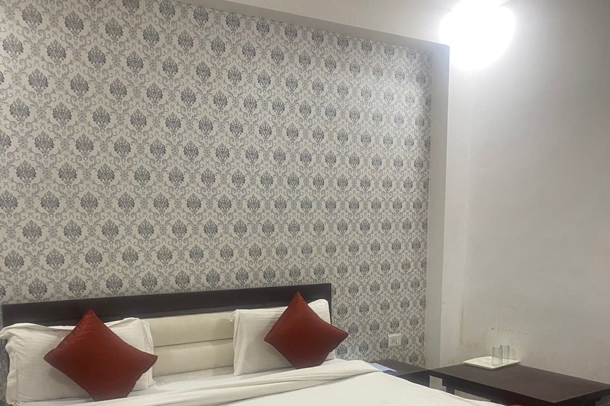 Cama bem arrumada com roupa de cama branca e vermelha, cabeceira escura e papel de parede estampado.