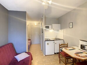 Un espace de vie compact comprenant une kitchenette, un coin repas et une petite chambre.