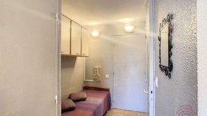 Un couloir étroit avec deux lits, un miroir et une porte.