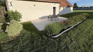 A building with a tiled roof, a patio with outdoor furniture, and a well-maintained garden.