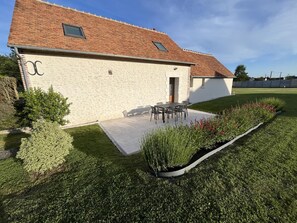 Ein Gebäude mit einem Ziegeldach, einer Terrasse mit Gartenmöbeln und einem gepflegten Garten.