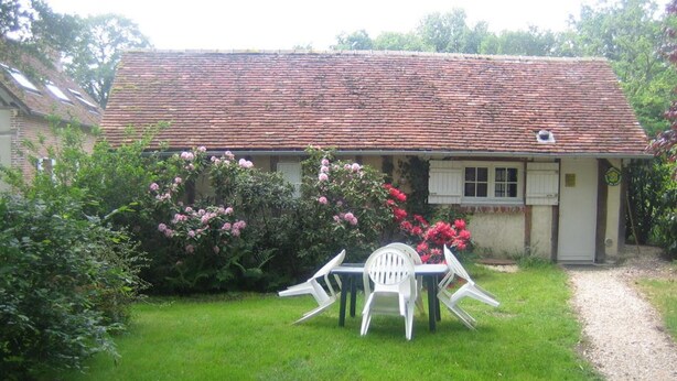 A house with a tiled roof, a garden with pink flowers, and a white table and chairs in the front yard. - Cottage with pond and boat, relaxation in Sologne (Saint-Viâtre)