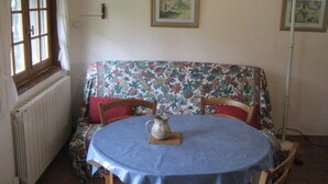 A dining area with a round table covered by a blue tablecloth, a floral sofa, and two chairs. A pitcher is placed on the table. - Cottage with pond and boat, relaxation in Sologne (Saint-Viâtre)