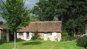A brick house with a tiled roof, surrounded by a well-maintained lawn and flowering plants. - Cottage with pond and boat, relaxation in Sologne (Saint-Viâtre)