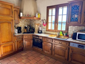 A kitchen with wooden cabinets, a tiled backsplash, a window with a view, and a microwave on the counter. - Luxury Lodge in Fontaines-en-Sologne: Heated Pool, Private Lake, Activities & Scenic Views (Fontaines-en-Sologne)