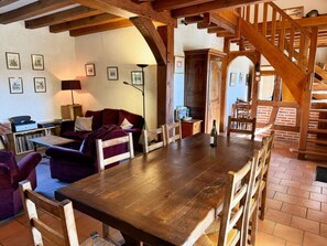 A rustic interior with a wooden dining table, a sofa, and a staircase.