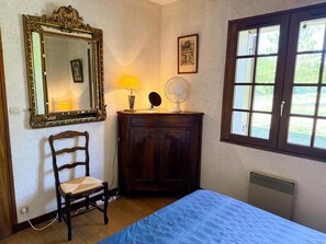 A bedroom with a bed, a chair, a dresser, a mirror, a window, and a wall-mounted fan. - Luxury Lodge in Fontaines-en-Sologne: Heated Pool, Private Lake, Activities & Scenic Views (Fontaines-en-Sologne)
