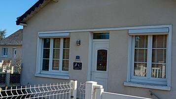 Un bâtiment à la façade beige, aux fenêtres à cadre blanc, doté d’une porte avec un panneau de verre et d’un portail en métal.