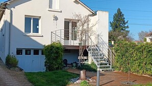 Una casa de dos pisos con un jardín delantero, una escalera de madera y barandilla metálica.