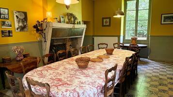 Une salle à manger avec une longue table, des chaises, une cheminée et une fenêtre donnant sur un paysage verdoyant.