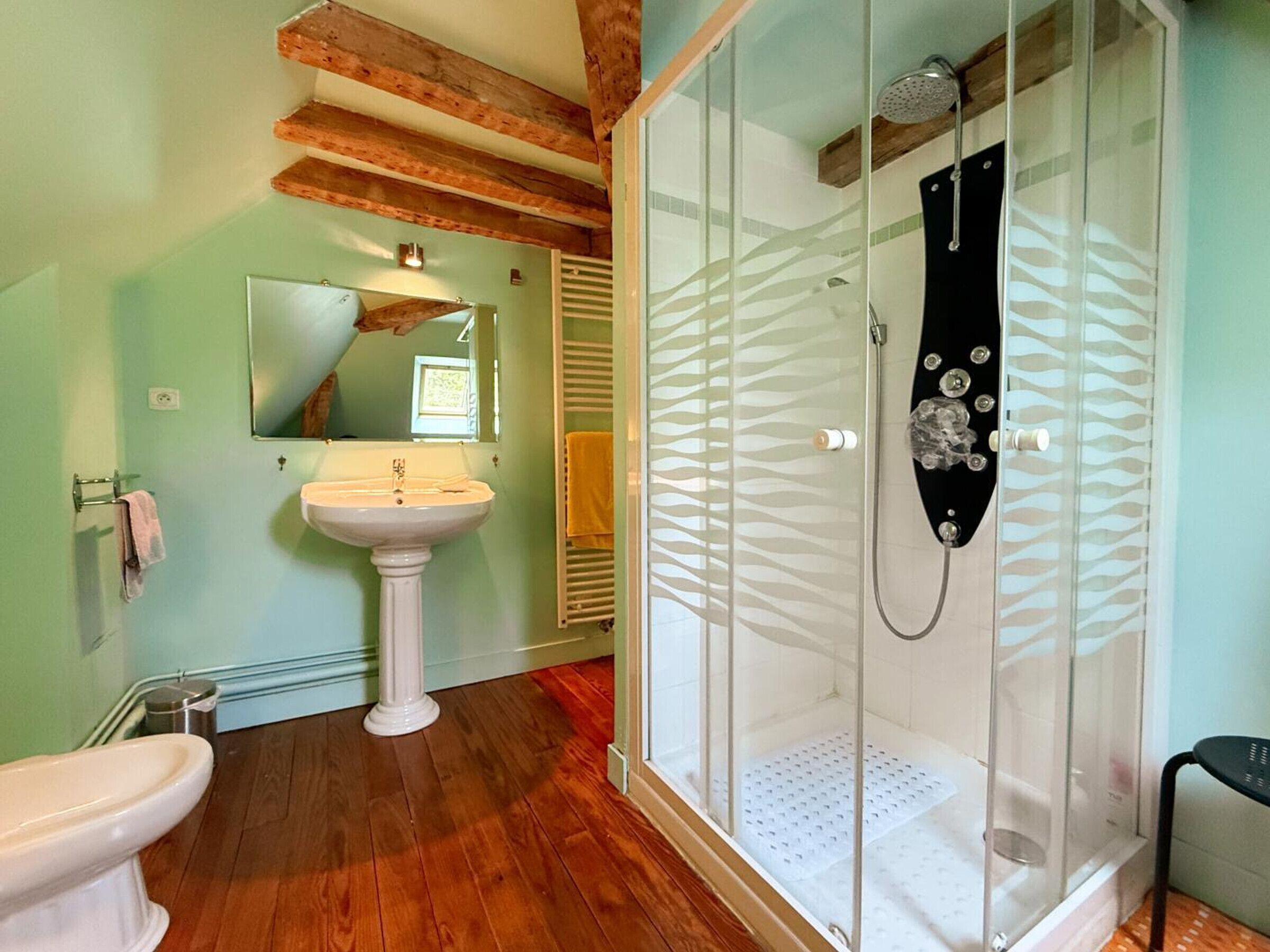 A bathroom with a pedestal sink, a toilet, a glass shower enclosure, and wooden beams on the ceiling.