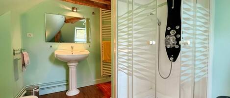 A bathroom with a pedestal sink, a toilet, a glass shower enclosure, and wooden beams on the ceiling.