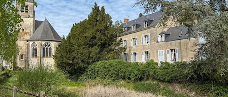 A historic building with a prominent tower, large windows, and a surrounding garden.