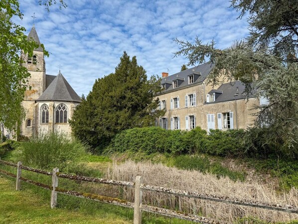 A historic building with a prominent tower, large windows, and a surrounding garden.