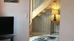 Una habitación con una escalera de madera, un cuadro de una escena callejera, una lámpara y un televisor.