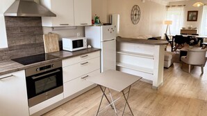 A modern kitchen with white cabinets, a built-in oven, a microwave, and a dining area with a table and chairs. - Cozy Renovated Cottage in Private Courtyard near Loire Castles (Avaray)