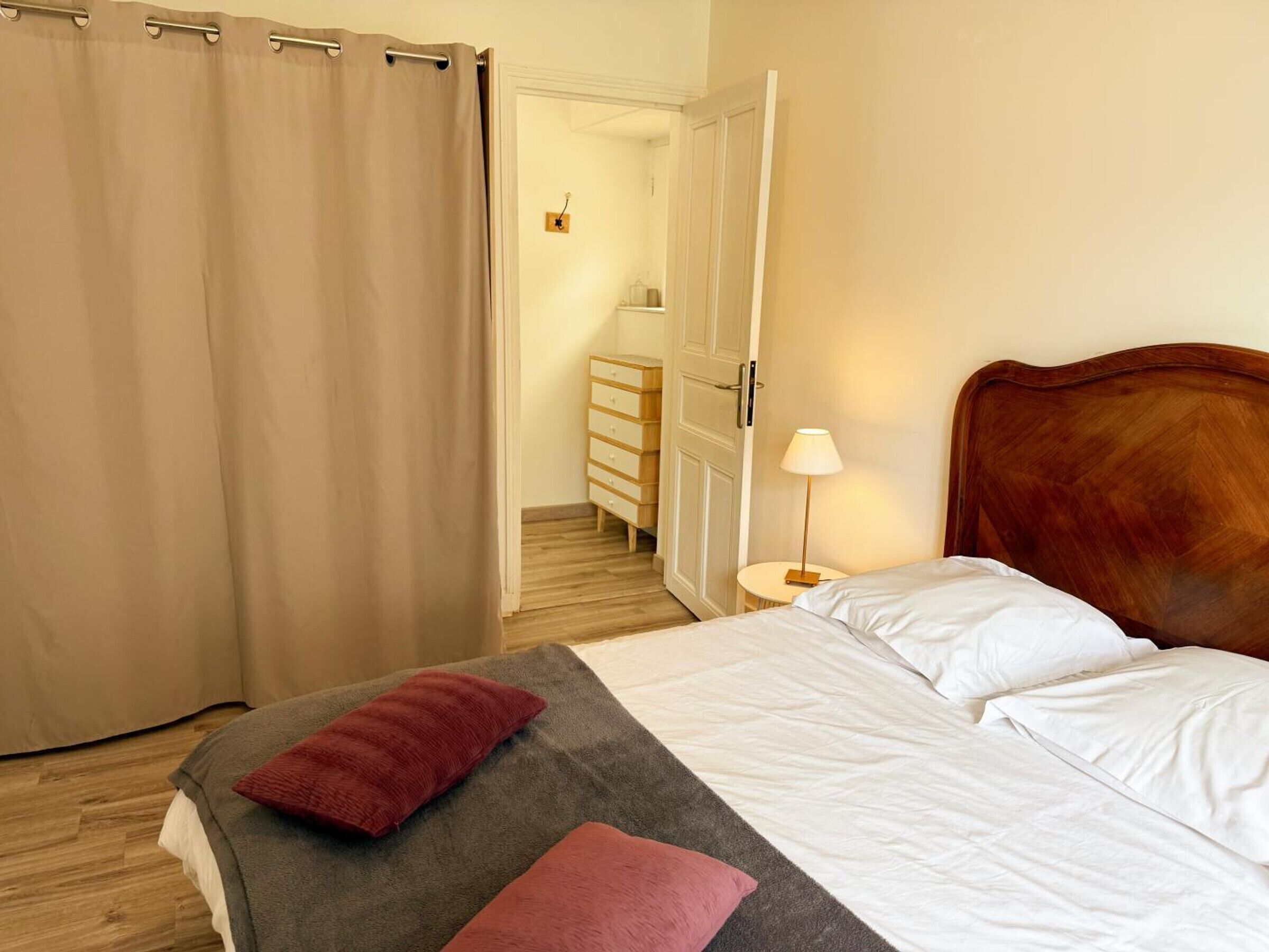 Een slaapkamer met een bed, kussens, een nachtkastje, een lamp en een houten hoofdeinde.