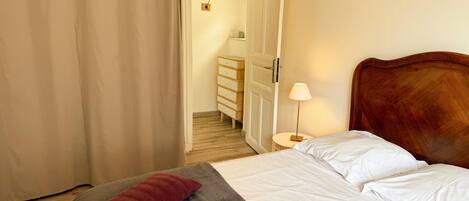 Een slaapkamer met een bed, kussens, een nachtkastje, een lamp en een houten hoofdeinde.