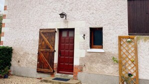 Un edificio rústico con puerta roja, una ventana pequeña y un portón de madera.
