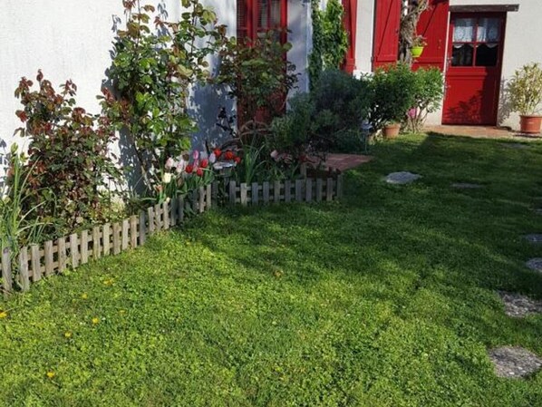 Un jardín cuidado con un seto de madera, diversas plantas y una puerta roja.