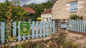 Un bâtiment en pierre avec un volet bleu, une clôture en bois et une enseigne indiquant qu’il s’agit d’un gîte en France.