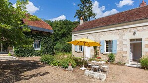 Une maison en pierre avec un toit de tuiles, un parasol jaune et une cour recouverte de gravier.