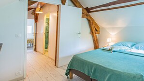 Une chambre avec un lit, une porte donnant sur une salle de bain et des poutres apparentes en bois au plafond.