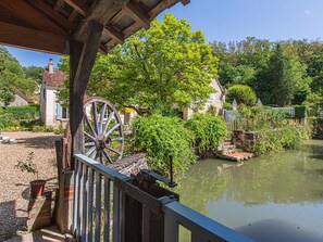 Un puente de madera rústico sobre un río tranquilo, rodeado de vegetación exuberante y edificios de piedra tradicionales.