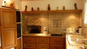 A kitchen with wooden cabinets, a brick fireplace, a tiled backsplash, and a countertop with various items. - Family home in Cheverny, enclosed garden, pets allowed, 6 people (Cheverny)