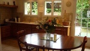 A kitchen with wooden cabinets, a round dining table, and chairs. There is a window with a view of greenery outside. - Family home in Cheverny, enclosed garden, pets allowed, 6 people (Cheverny)