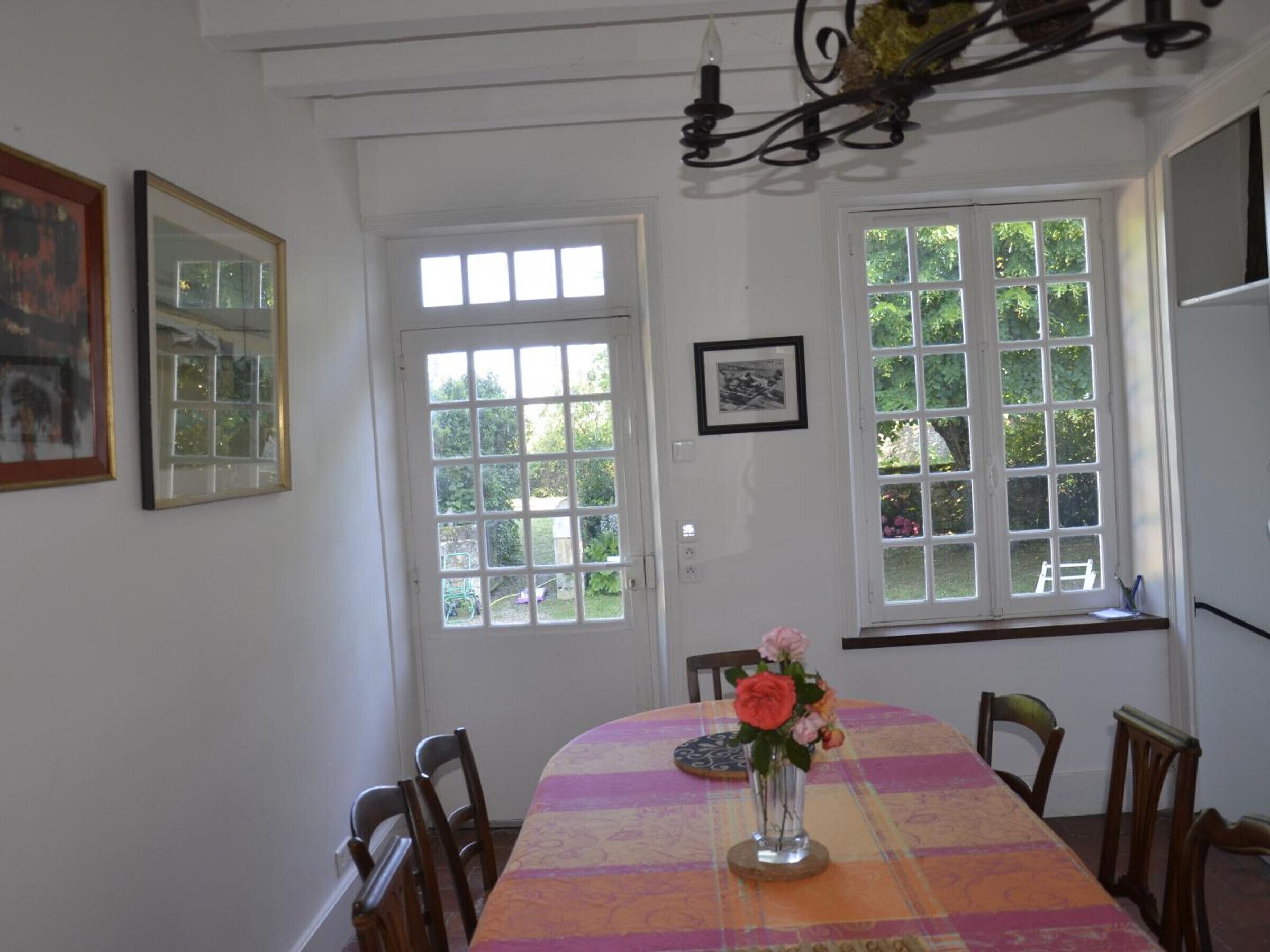 A dining area with a table set for four, a vase with flowers, and a window with a view of greenery.