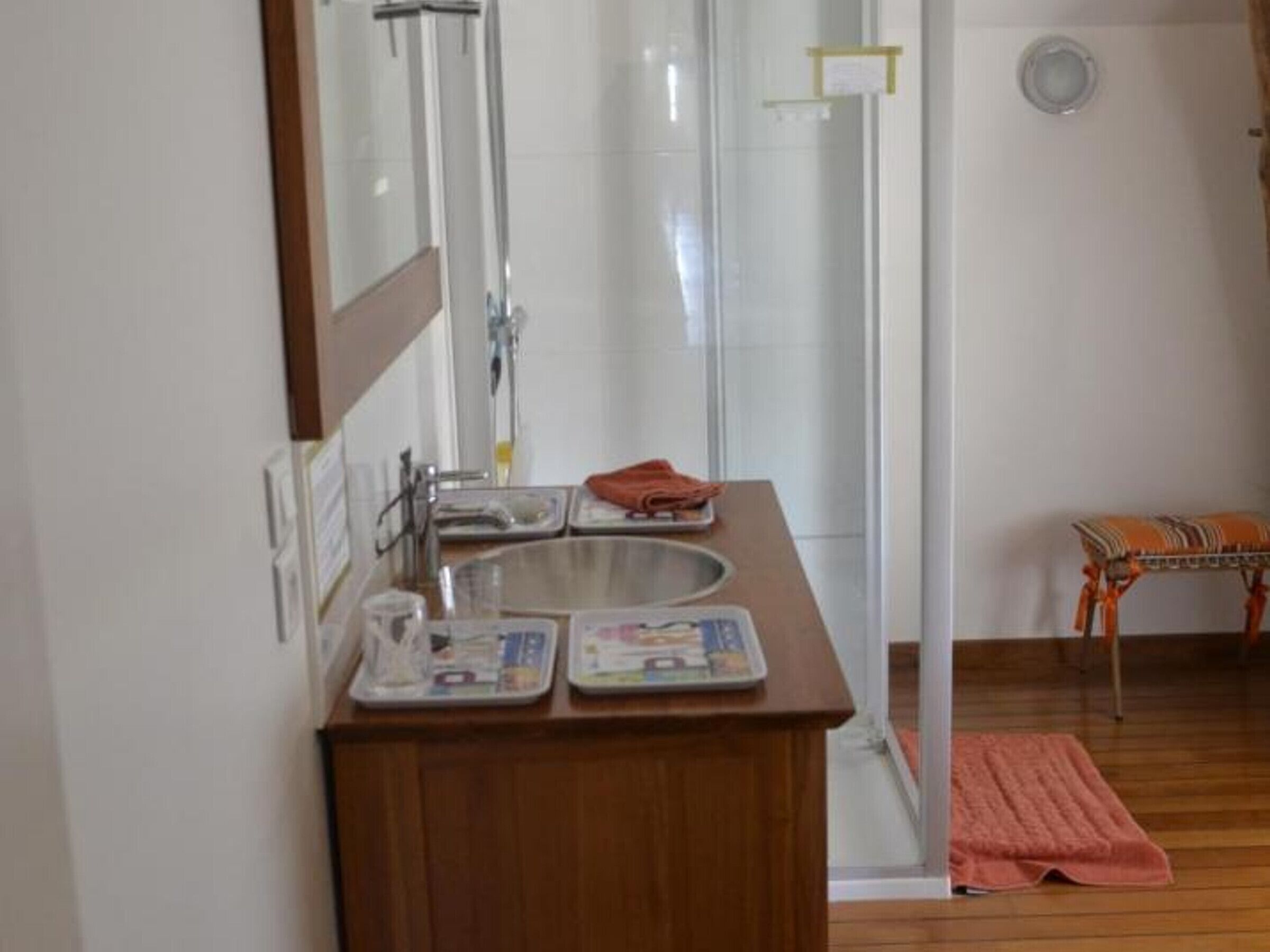 A bathroom with a wooden vanity, a mirror, a sink, and a shower area.