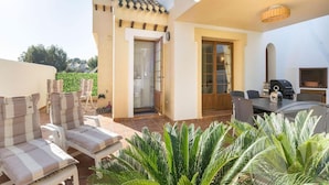 A patio area with outdoor seating, a grill, and a door leading to a covered entrance. - La Manga Club Monte Claro Townhouse 606 (Atamaría)