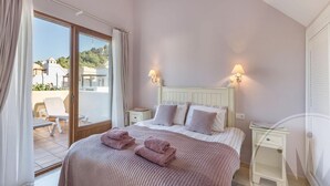 A bedroom with a bed, two bedside tables, a window with curtains, and a view of the outside. - La Manga Club Monte Claro Townhouse 606 (Atamaría)