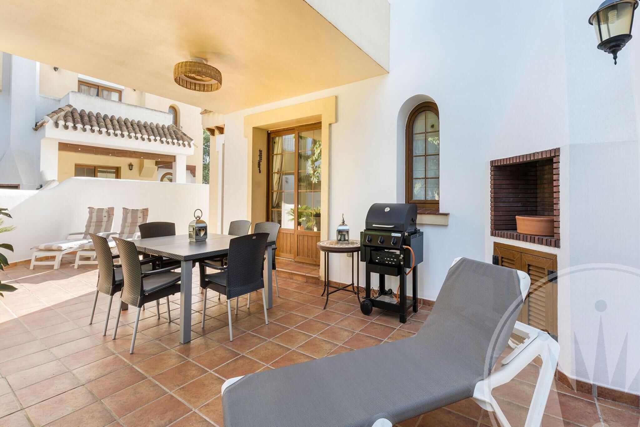 Eine Terrasse mit Esstisch, Stühlen, Grill und Liegestuhl.