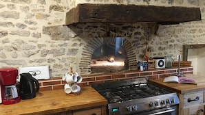 Una cocina con pared de piedra, horno de ladrillo, estufa a gas y armarios de madera.