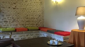 Un muro de piedra, una mesa con una bandeja de tazas y una lámpara sobre una mesita auxiliar.
