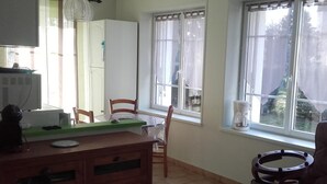 A small kitchen with a refrigerator, a wooden cabinet, a dining table with chairs, and a window with curtains. - One-story house with park near Beauval Zoo (Meusnes)