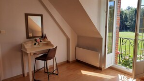 A bedroom with a sloped ceiling, a wooden desk with a chair, a large window, and a view of a garden. - Family Retreat with Private Pool, Games, and Farm Animals in the Countryside (Danzé)