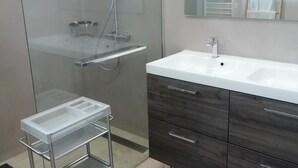 A modern bathroom with a glass shower enclosure, a white sink, and a vanity with dark wood drawers.