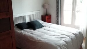 A bedroom with a bed, a bedside table with a lamp, and a window with curtains.