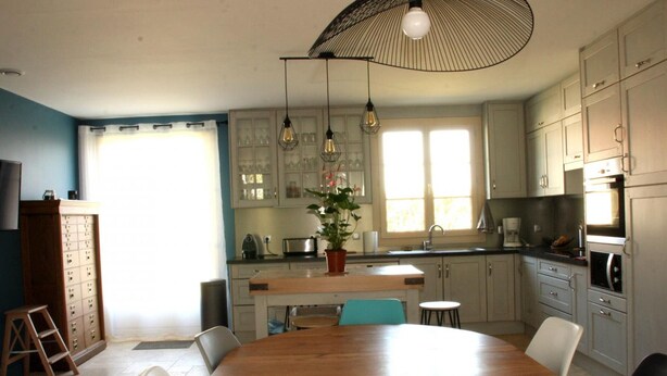 A kitchen with a wooden dining table, light-colored cabinets, and a large window.