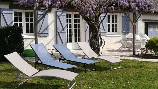 A building with a tiled roof, a tree with purple flowers, and four lounge chairs in the foreground. - Family cottage in the heart of the Loire Castles (Oisly)