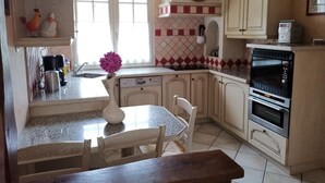 A kitchen with a dining table, chairs, a clock, and a stove. - Family cottage in the heart of the Loire Castles (Oisly)