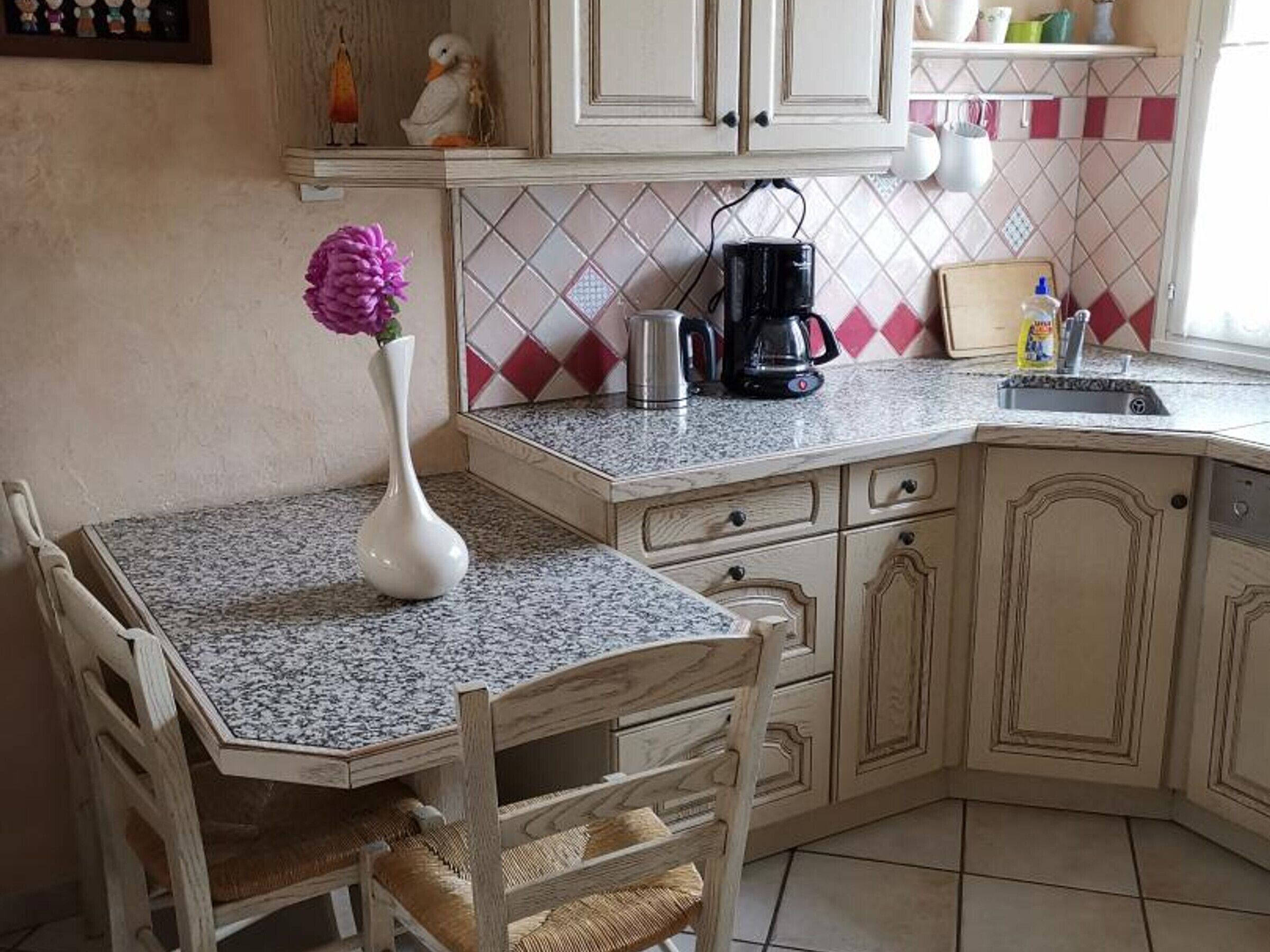 Une cuisine dotée d’un plan de travail en granit, de meubles blancs, d’une machine à café et d’un vase rempli de fleurs.