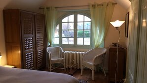 A bedroom with a large bed, two wicker chairs, a radiator, and a window with curtains. - Charming Renovated House with Garden, Near Loire Valley Castles (Dhuizon)