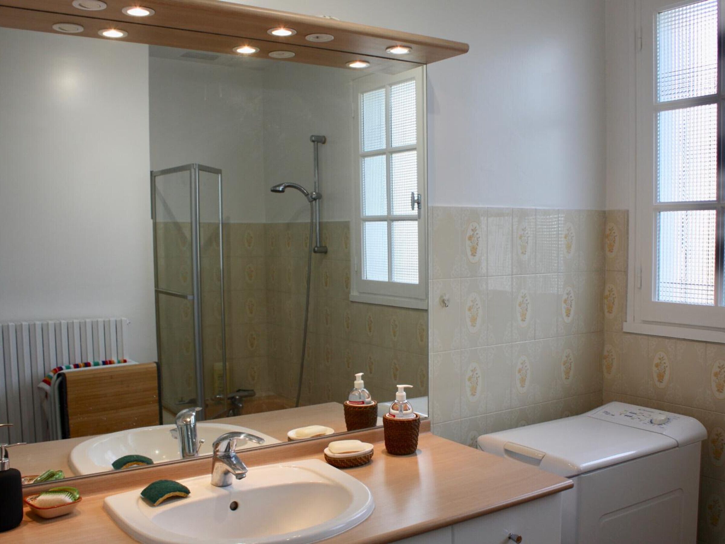 A bathroom with a large mirror, a sink, a shower, and a toilet.