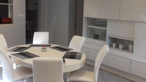Een moderne eetruimte met een ronde tafel en witte stoelen, een witte kast met glazen deuren en een rood voorwerp erboven.
