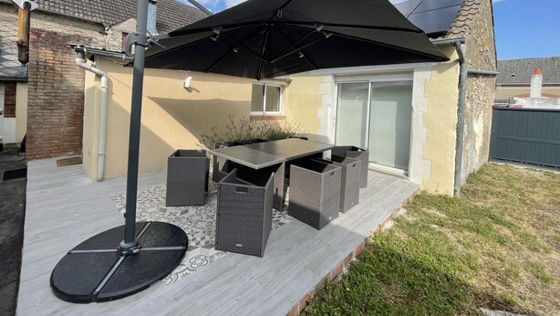 Een terras buiten met een tafel, stoelen, een grote parasol en een pergola.