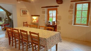 Comedor con una mesa dispuesta para seis comensales, sillas de madera, una lámpara y una computadora sobre un escritorio.